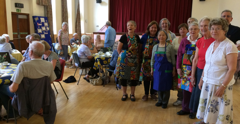 Members of Christ Church Southgate having lunch with the committee dressed in colourful Rwanda aprons