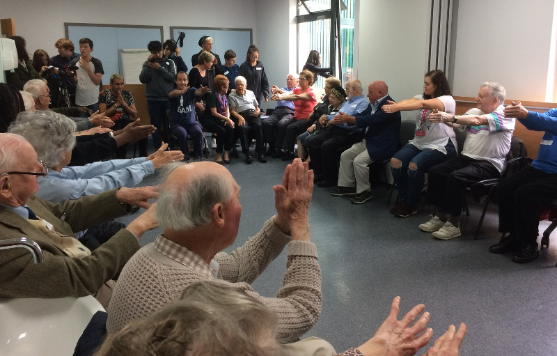 Members of Dementia Club UK doing their chair exercises watched by students from NCS